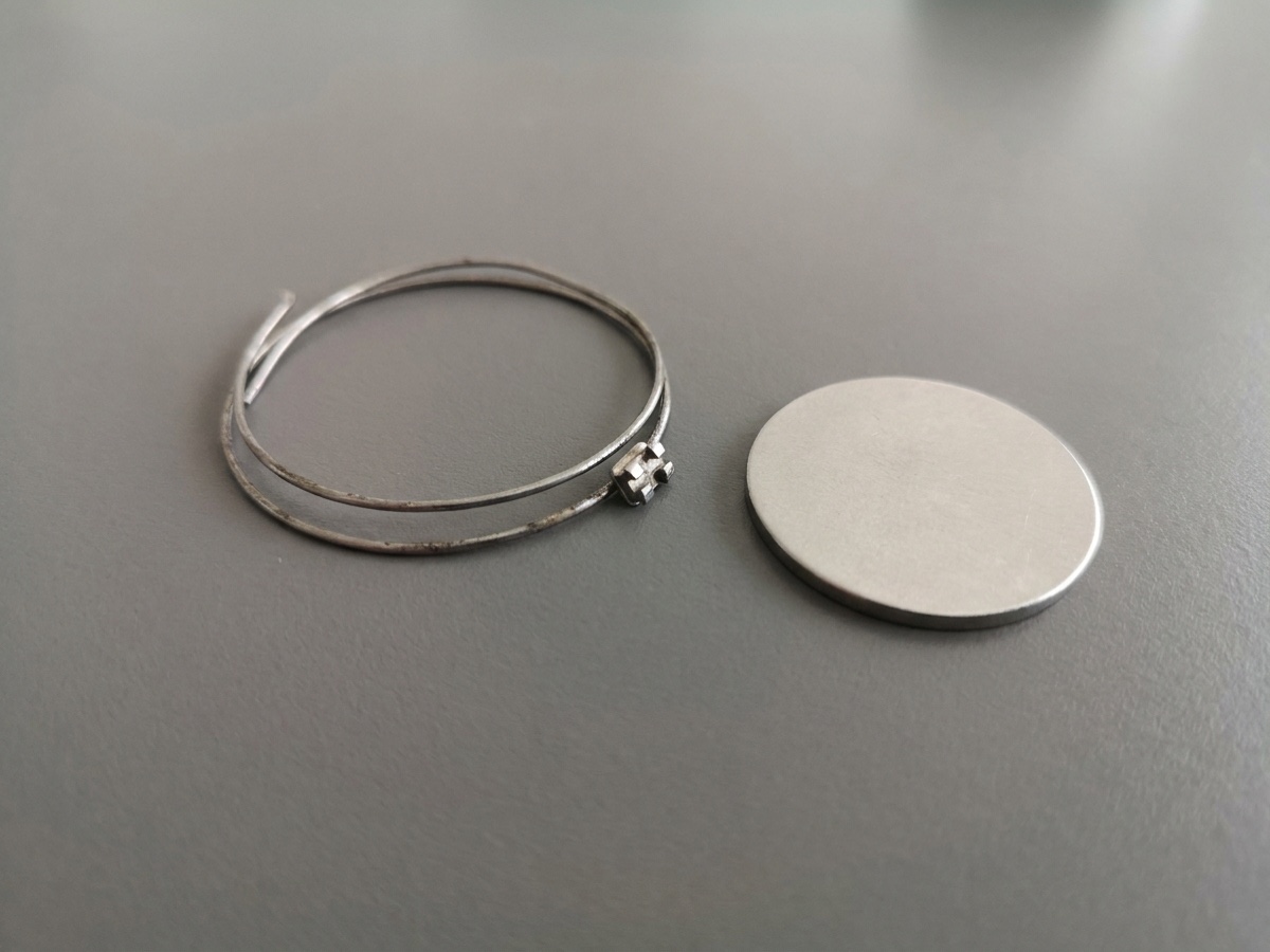 Retainer wire and a small orthodontic attachment beside a coin-sized object for scale